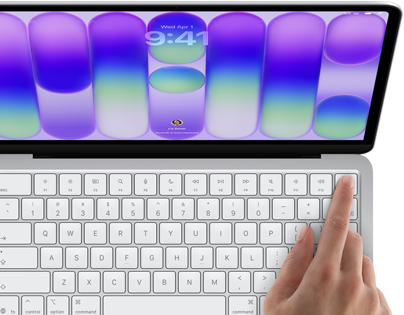 MacBook Neo, stříbrná barva, zobrazuje se přihlašovací obrazovka, něčí prst na snímači Touch ID v pravém horním rohu klávesnice